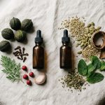 Two amber dropper bottles on linen, one surrounded by black walnut, clove, wormwood, hawthorn and garlic, the other by fennel, pumpkin seed, bark, peppermint and oregano