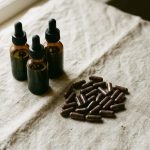 Three unlabelled amber dropper bottles and a scatter of dark capsules on pale linen